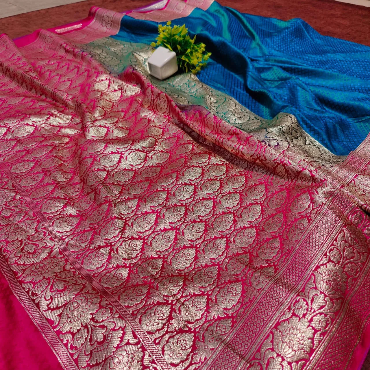 saree for women
A luxurious Banarasi silk saree displayed on a mannequin, featuring a rich combination of pink, blue, and gold tones. The saree is adorned with intricate gold zari weaving in traditional floral and geometric patterns, with a broad golden border adding elegance. The vibrant color gradient enhances its beauty, making it perfect for festive and wedding occasions.