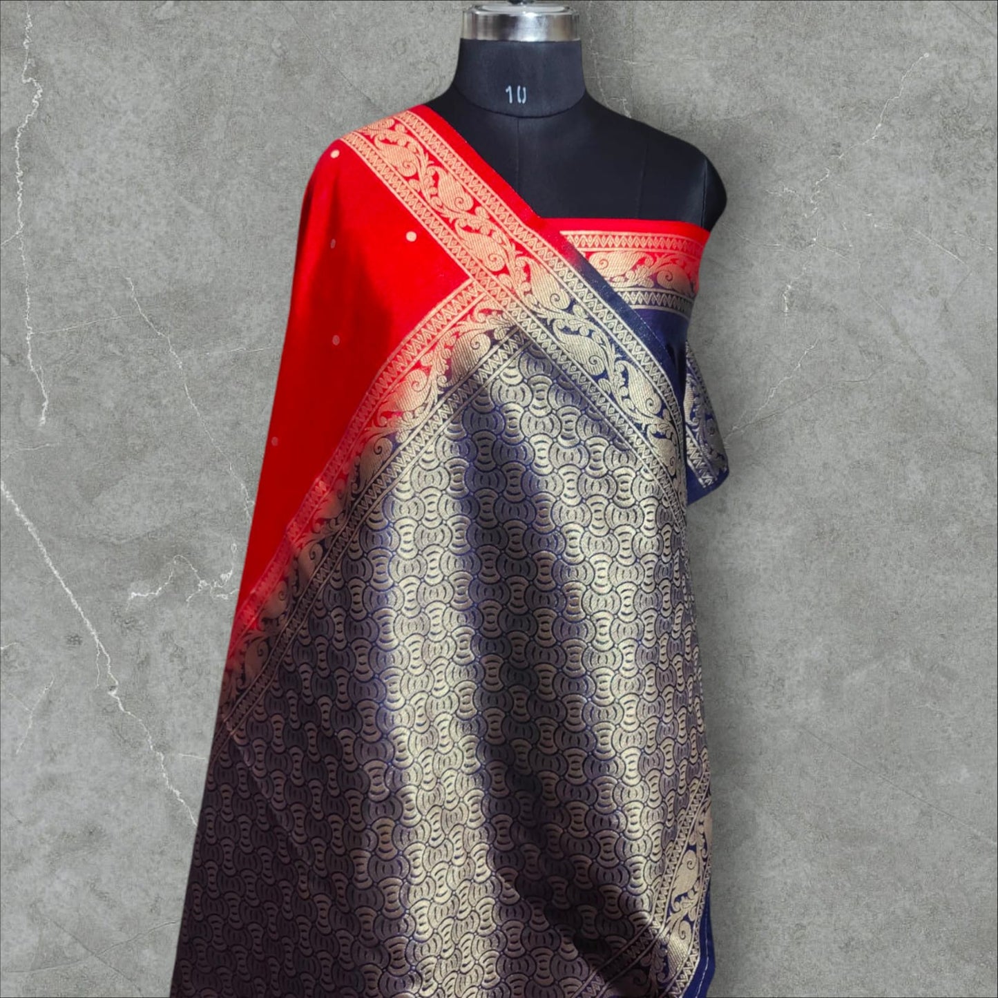 A vibrant saree with a striking combination of colors and intricate patterns. The upper part features a rich red base with small white dots, followed by a checkered design in shades of pink, purple, orange, and green, each square adorned with delicate floral motifs. The lower part and pallu contrast beautifully with a gray and navy blue intricate wave-like pattern, bordered with elegant floral and vine motifs. The saree blends traditional and contemporary aesthetics,