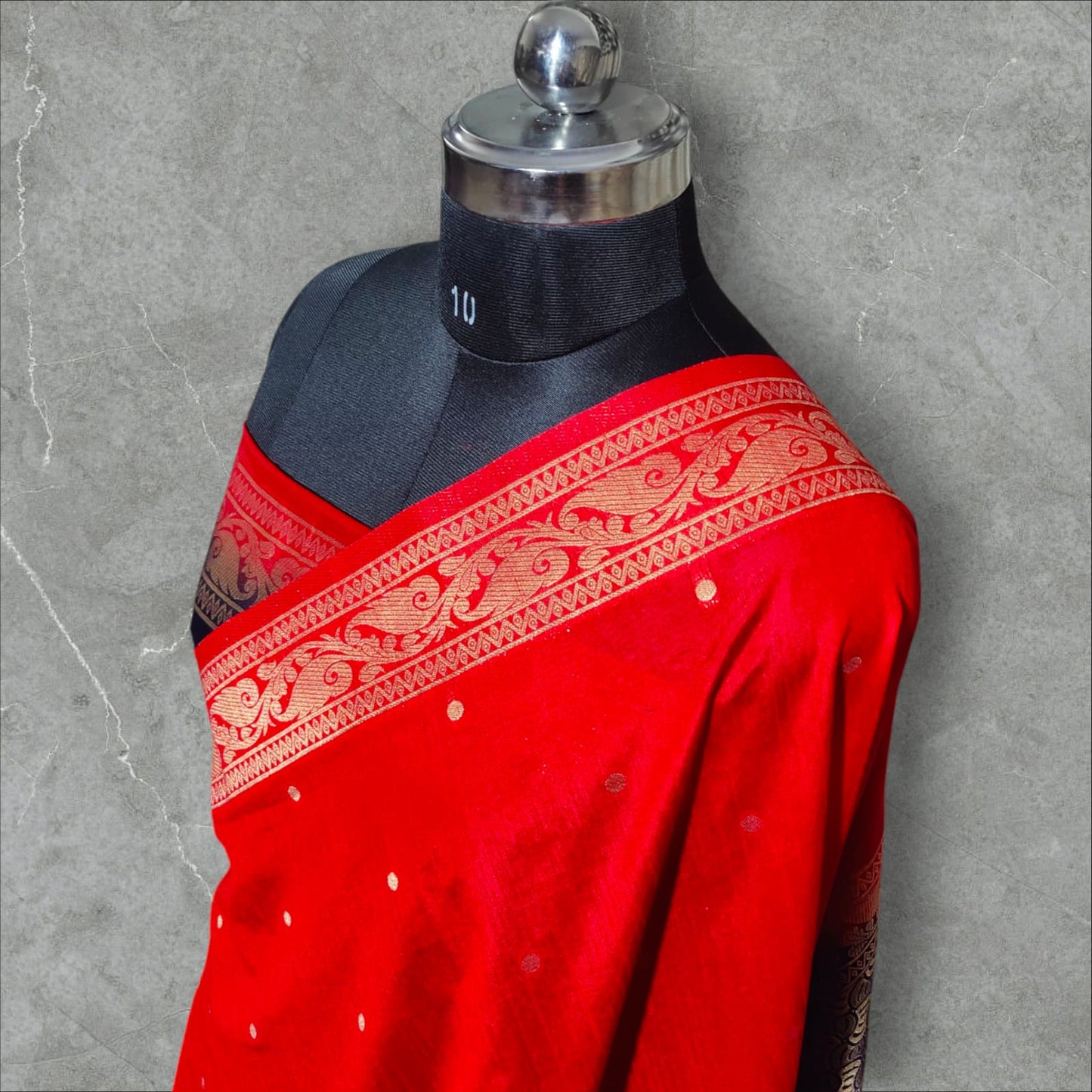 A vibrant saree with a striking combination of colors and intricate patterns. The upper part features a rich red base with small white dots, followed by a checkered design in shades of pink, purple, orange, and green, each square adorned with delicate floral motifs. The lower part and pallu contrast beautifully with a gray and navy blue intricate wave-like pattern, bordered with elegant floral and vine motifs. The saree blends traditional and contemporary aesthetics, making it perfect for festive
