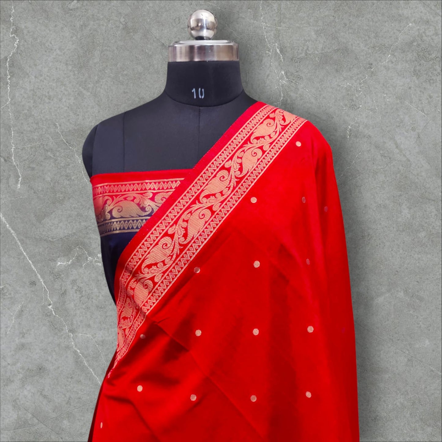 A vibrant saree with a striking combination of colors and intricate patterns. The upper part features a rich red base with small white dots, followed by a checkered design in shades of pink, purple, orange, and green, each square adorned with delicate floral motifs. The lower part and pallu contrast beautifully with a gray and navy blue intricate wave-like pattern, bordered with elegant floral and vine motifs. The saree blends traditional and contemporary aesthetics, making it perfect for festive