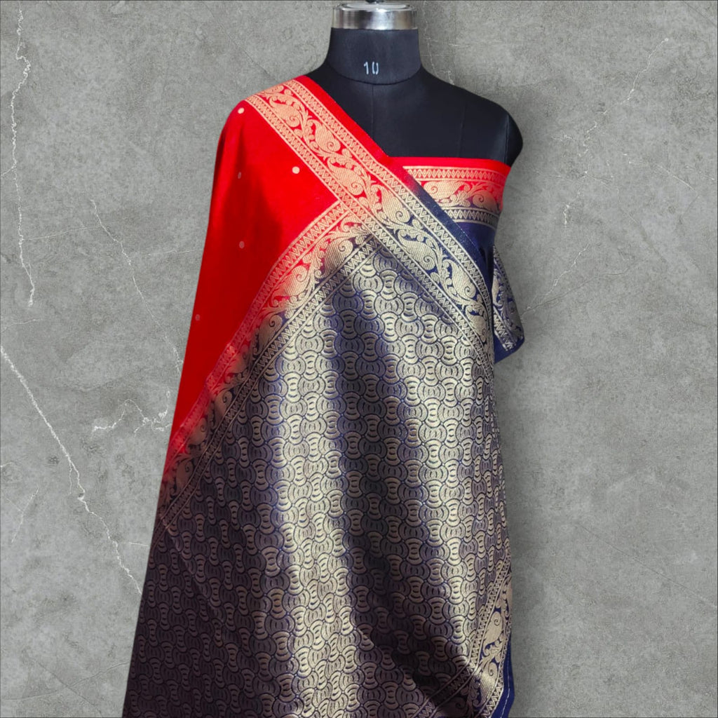 A vibrant saree with a striking combination of colors and intricate patterns. The upper part features a rich red base with small white dots, followed by a checkered design in shades of pink, purple, orange, and green, each square adorned with delicate floral motifs. The lower part and pallu contrast beautifully with a gray and navy blue intricate wave-like pattern, bordered with elegant floral and vine motifs. The saree blends traditional and contemporary aesthetics, 